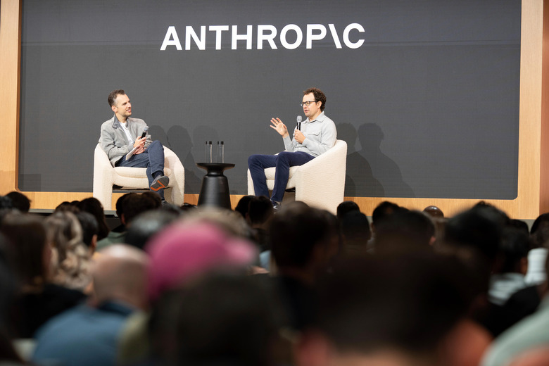 Two men in an on-stage conversation seated in white armchairs in front of a large screen displaying the Anthropic logo, with an audience seated in the foreground.