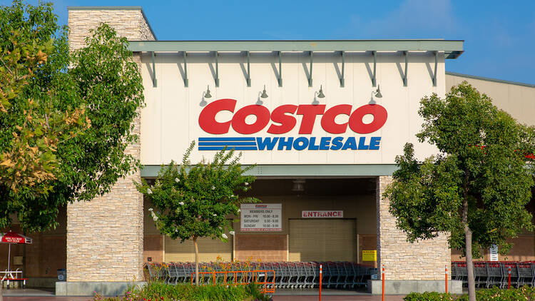 Costco warehouse storefront with customers and shopping carts outside.