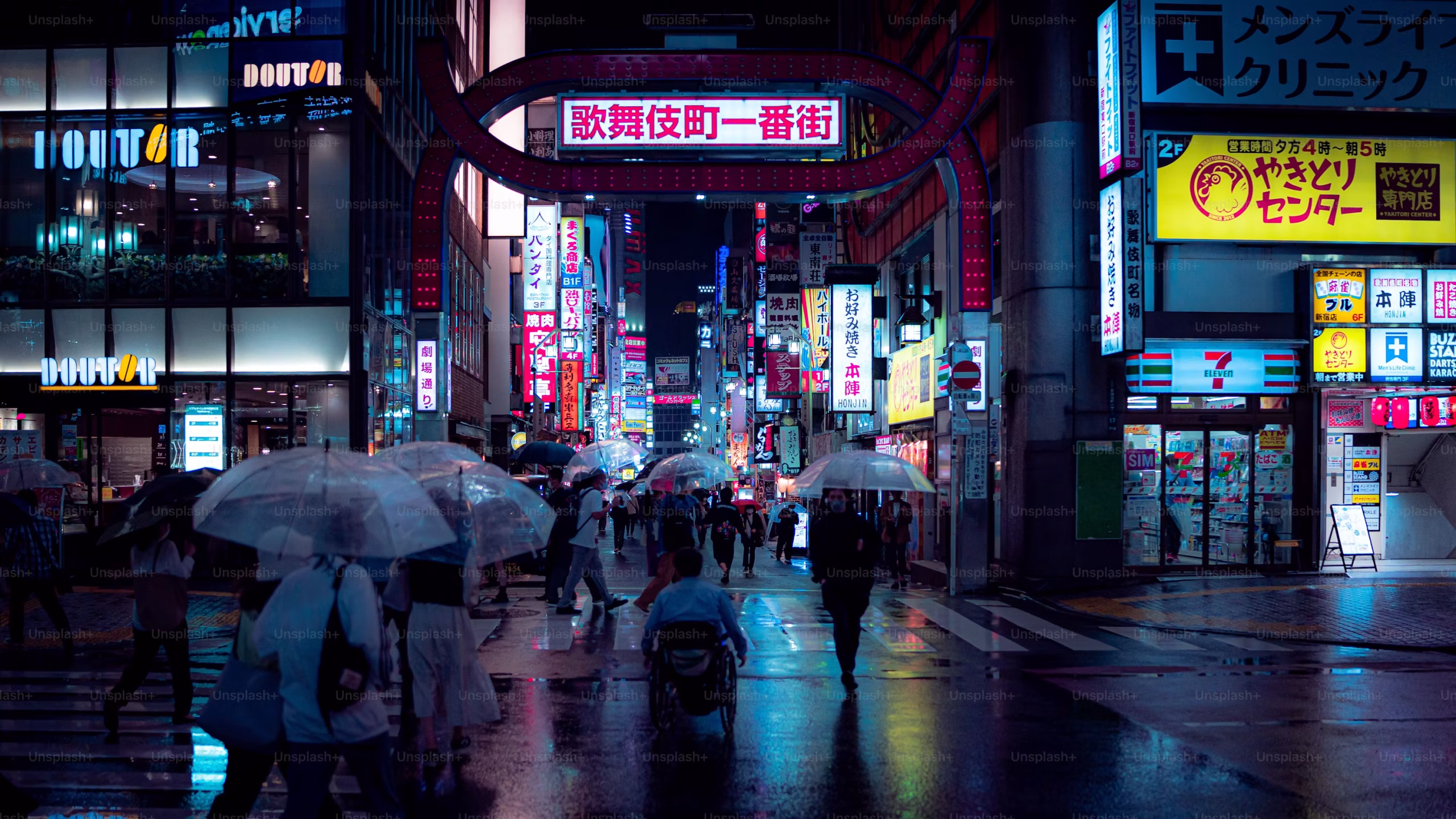 Rain-soaked street in Tokyo, Japan, with pedestrians carrying umbrellas beneath illuminated signs.